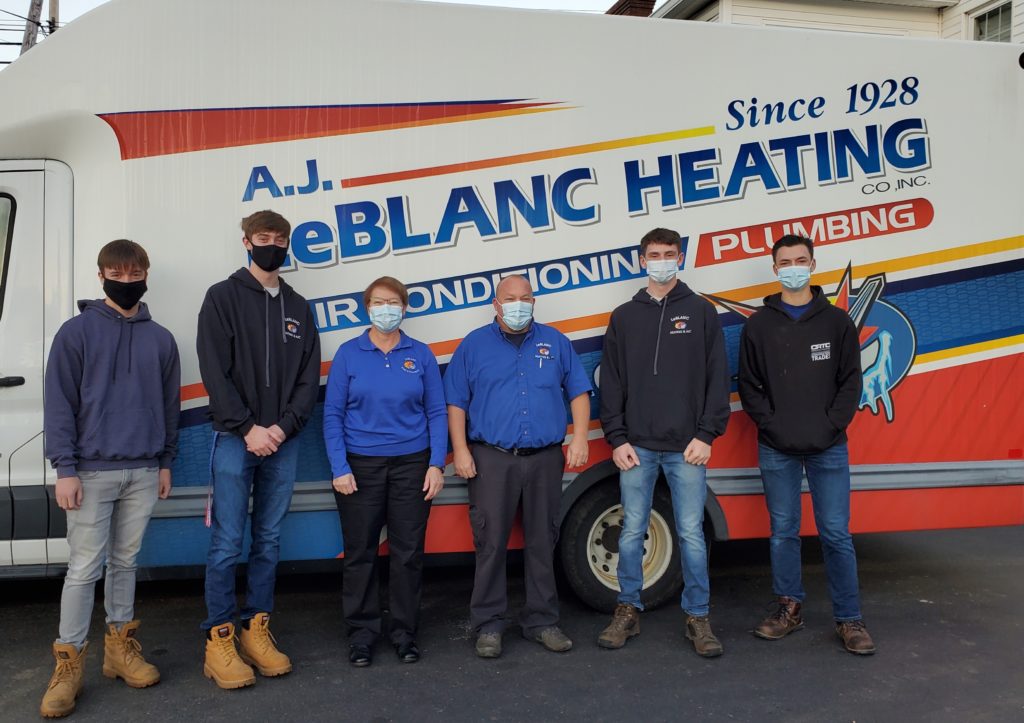 Six people wearing masks stand in front of a LeBlanc Heating company van parked on a street.
