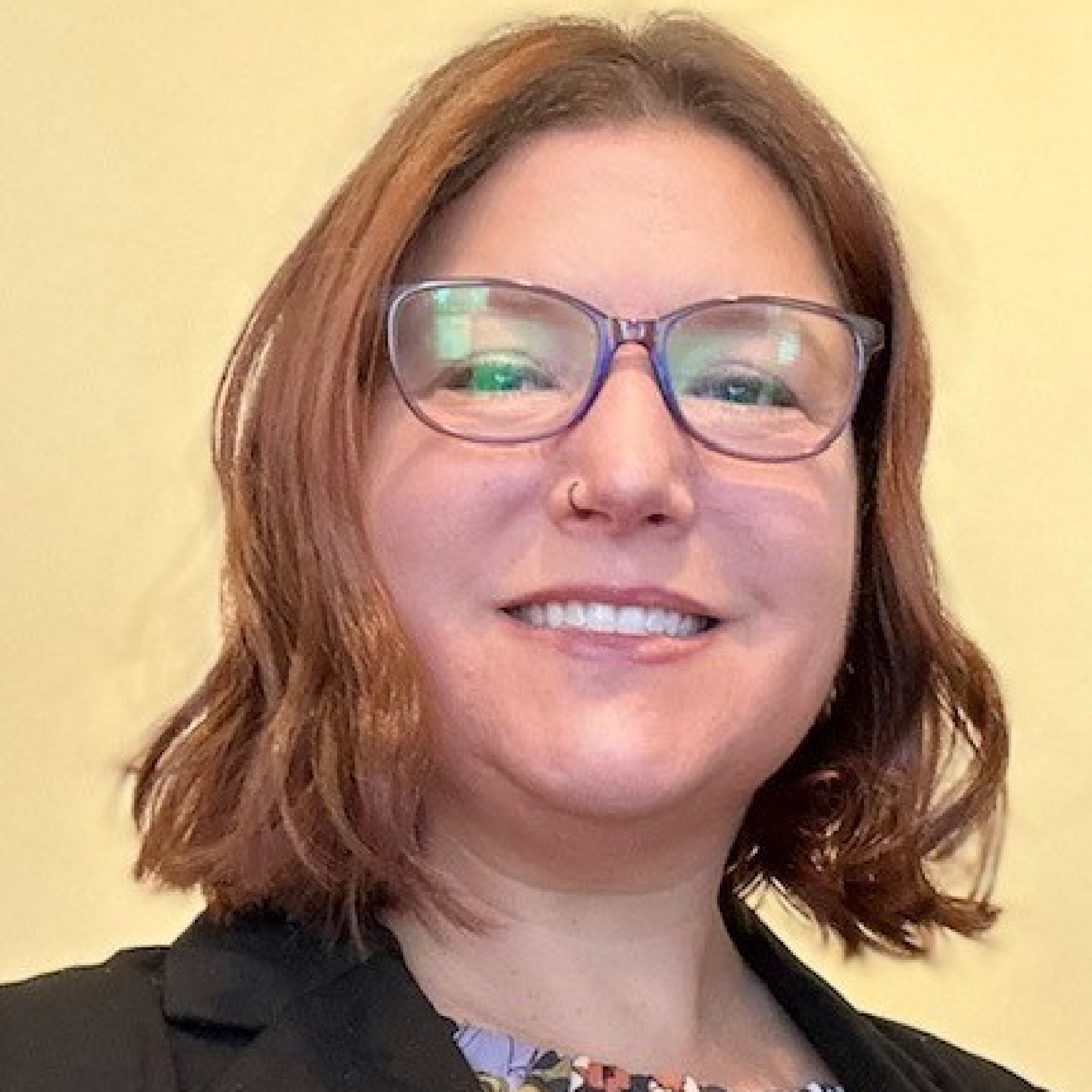 Karyn Yeatman. Smiling woman with glasses and shoulder-length brown hair, wearing a black blazer, in front of a plain background.