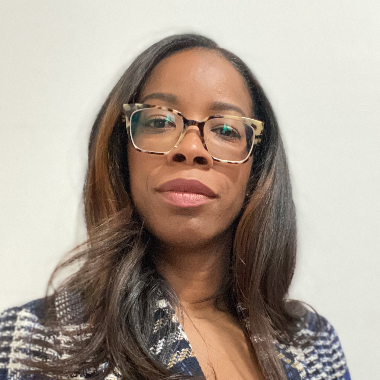 Woman with long dark hair, glasses, and a checkered jacket poses against a plain white background.