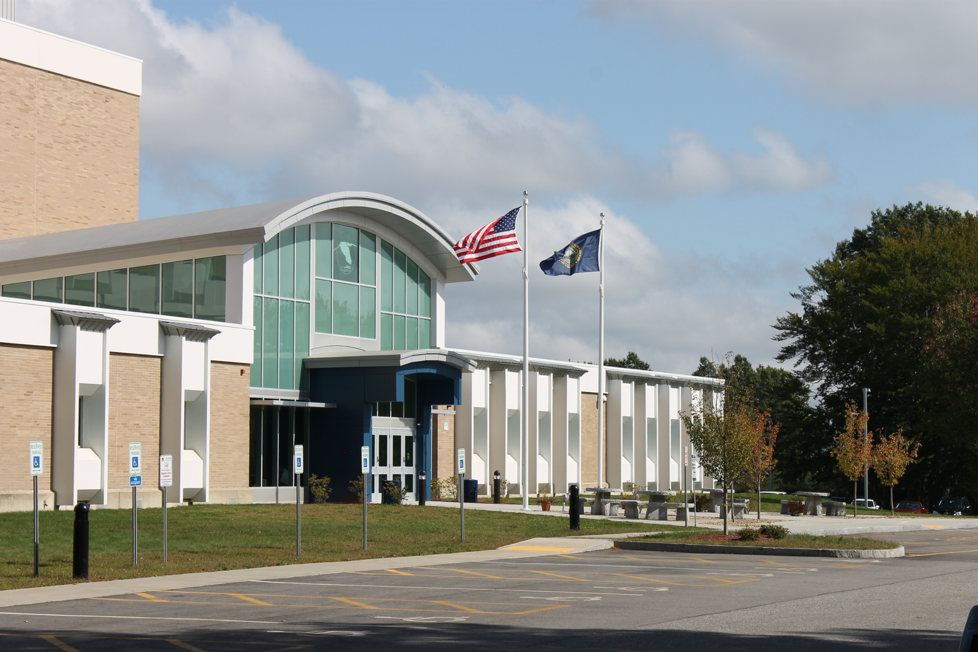 Modern school building with glass entrance, American and state flags, and a mostly empty parking lot.