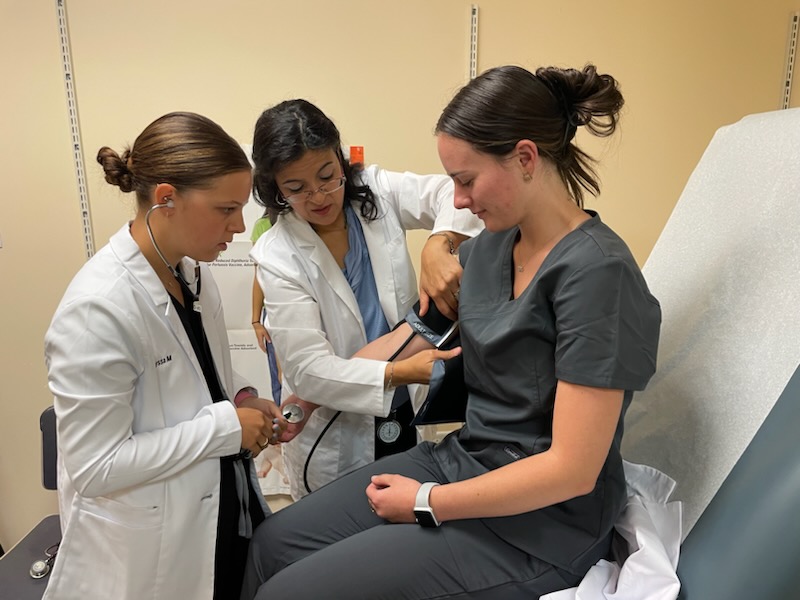 Two healthcare professionals check a patients blood pressure in a medical examination room.